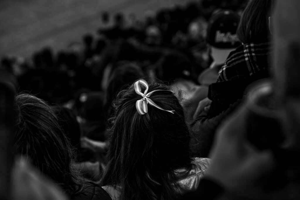 A black and white photograph focusing on a hair bow amidst a crowd, conveying a sense of individuality.