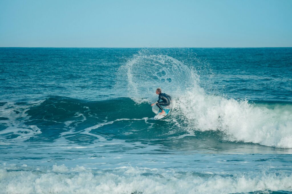A surfer skillfully rides a powerful ocean wave on a clear sunny day.