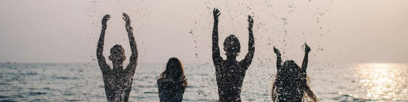 Silhouettes of four people joyfully splashing water in the sea during a beautiful sunset.